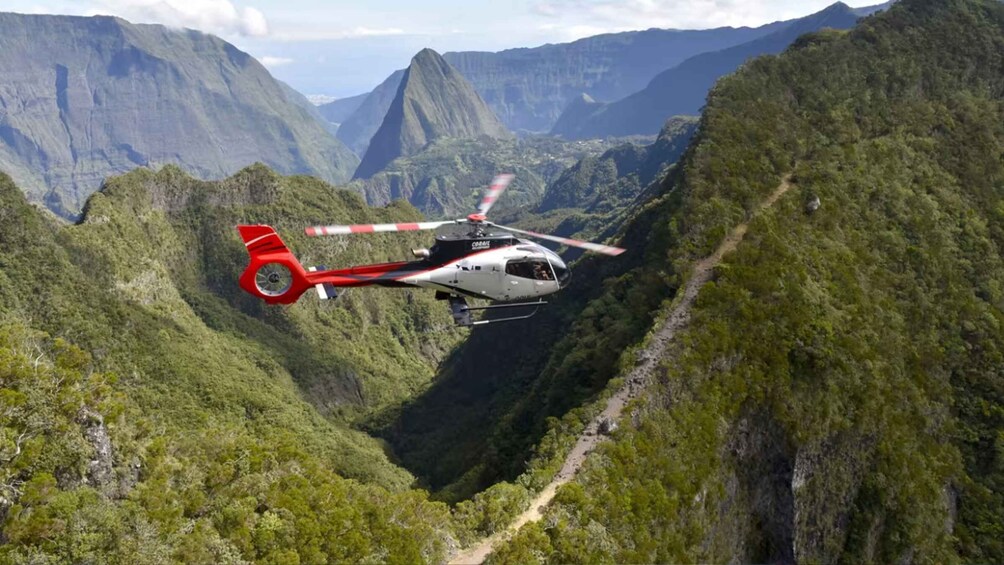 A helicopter flying over a lush green valley with steep cliffs. 2