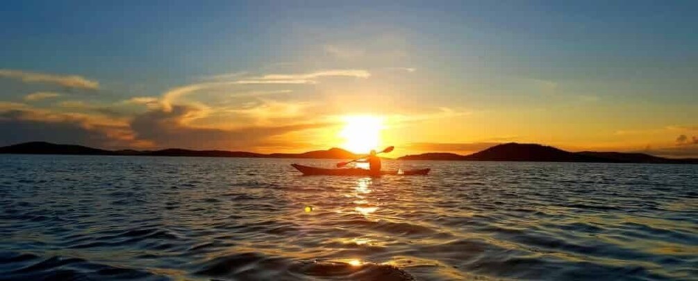 A sunset over a calm sea with a boat and a person paddling. 2