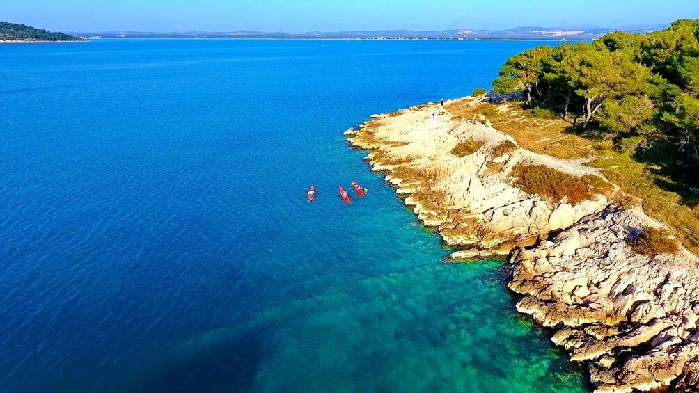 A coastal landscape with clear blue waters, rocky cliffs, and dense green foliage. 4