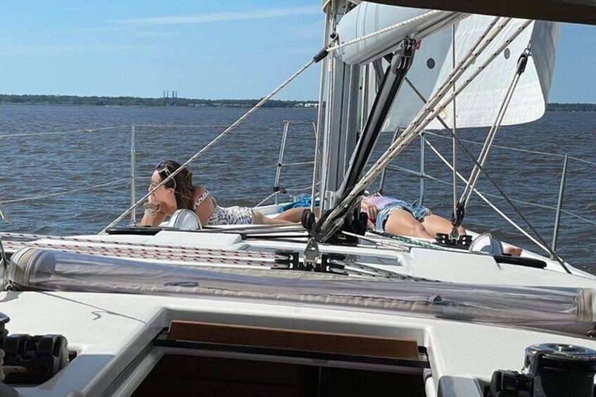 A sailboat with two people lying on the deck, a mast, and calm water in the background. 4