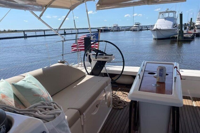 A boat deck with a cushioned seating area, a steering wheel, and an American flag. 1