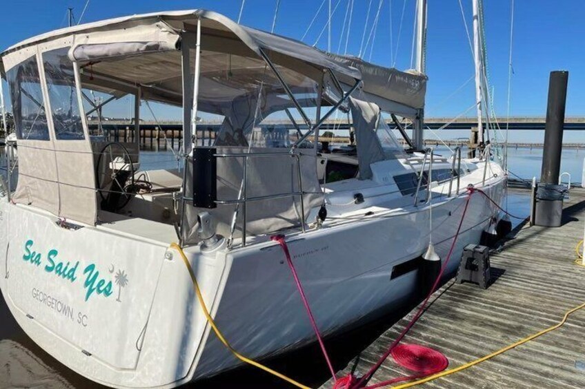 A sailboat docked at a pier with a clear sky and a bridge in the background. 4