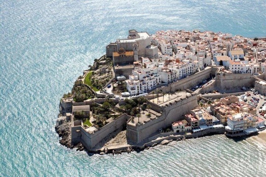 An aerial view of a coastal town with a fortified structure, dense buildings, and a clear blue sea. 4