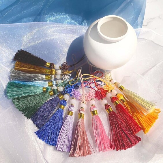 A variety of colorful tassels and beads arranged on a white surface with a white vase in the background. 1