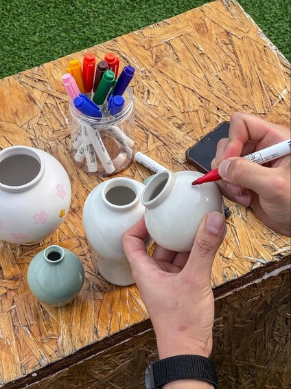 Hands painting ceramic pots with markers on a wooden table. 4