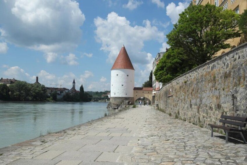 A cobblestone pathway beside a river, a stone wall, and a white tower with a red roof. 4