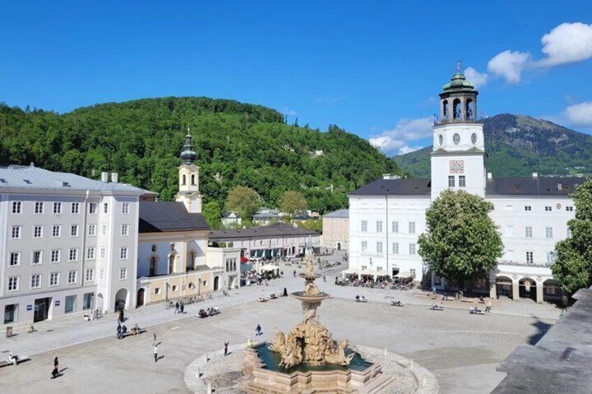 A town square with a fountain, historic buildings, and a church with a bell tower. 1