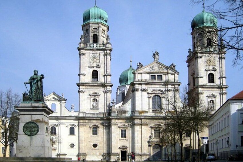 A historic church with three domes and a statue in front. 5