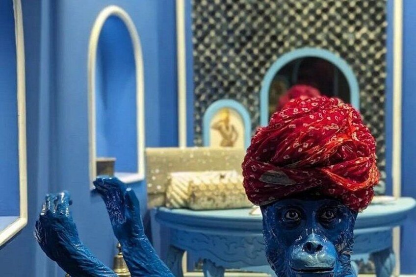 A blue statue with raised hands in a room with blue walls and a patterned wall behind it. 3