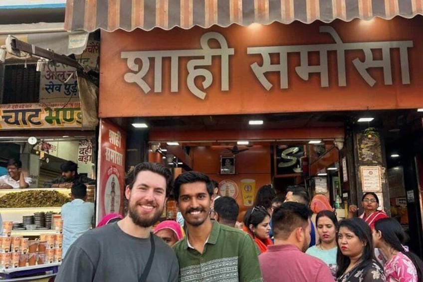 A busy street scene with a shop named 'Shahi Samosa' and people gathered around. 3