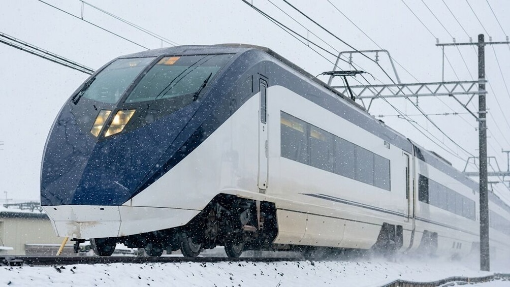 A high-speed train on tracks with overhead power lines, snow falling, and a snowy landscape. 1