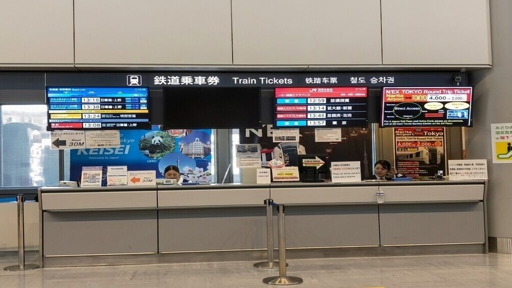 A train ticket counter with digital displays and signs for train schedules and ticket prices. 5