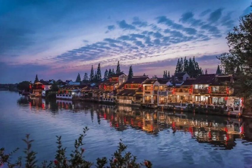 A waterfront with illuminated buildings reflecting on the water at dusk. 2