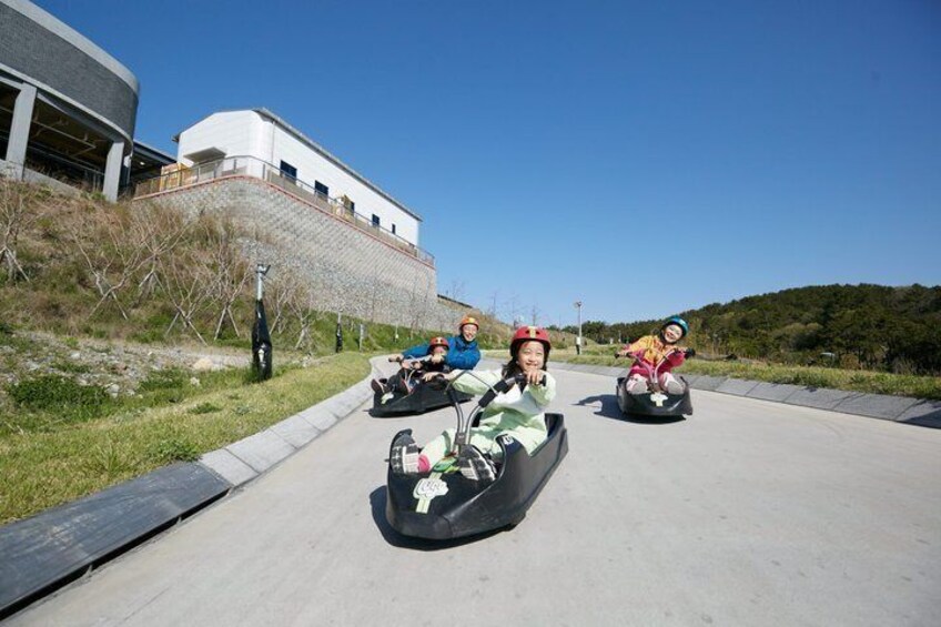 People in go-karts on a track with a building in the background. 1