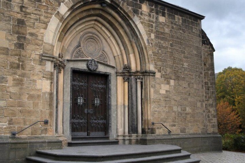 A stone building with a large arched entrance, a clock, and steps leading up to the door. 2