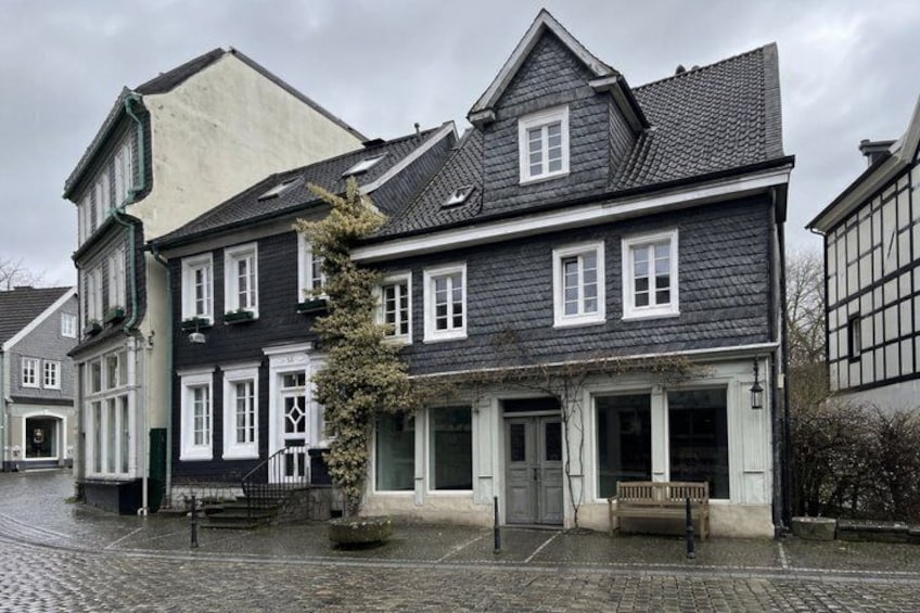 A cobblestone street lined with historic buildings, a bench, and a tree. 3