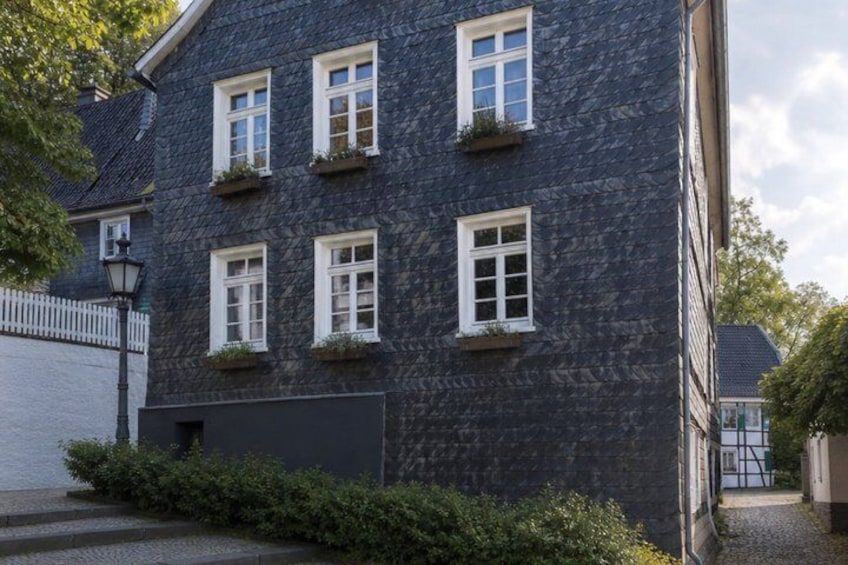 A dark stone building with multiple windows, some with flower boxes, and a white picket fence in the background. 4