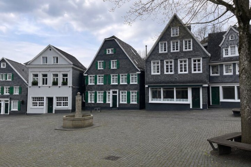 A courtyard with traditional European buildings, a central fountain, and cobblestone pavement. 5