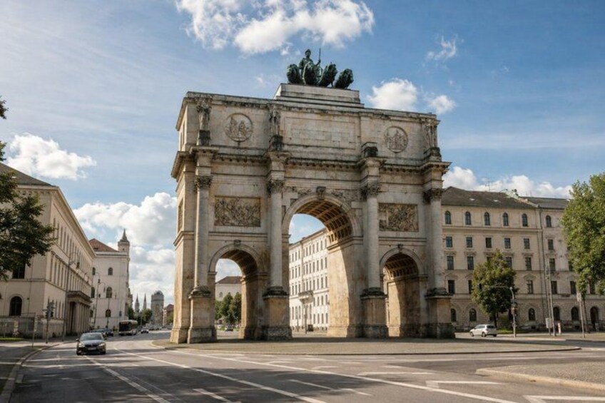 A large stone archway with statues on top, surrounded by buildings and a clear sky. 2