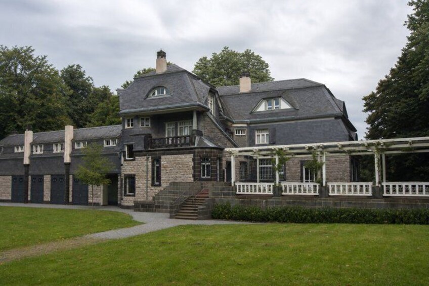 A large, historic house with a stone facade, multiple chimneys, and a covered porch. 2