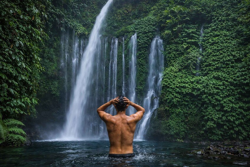 A man standing in water with waterfalls in the background. 1