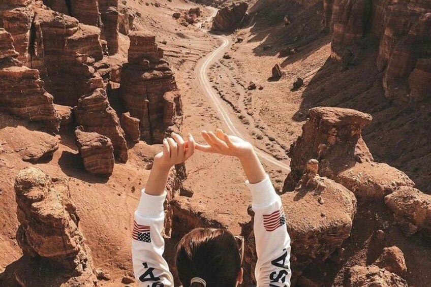 A person standing on a rocky outcrop with arms raised, overlooking a winding road through a canyon. 4