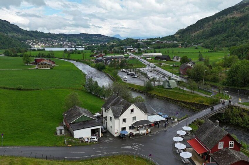 A rural landscape with a river, green fields, a bridge, and a white building with a red roof. 3