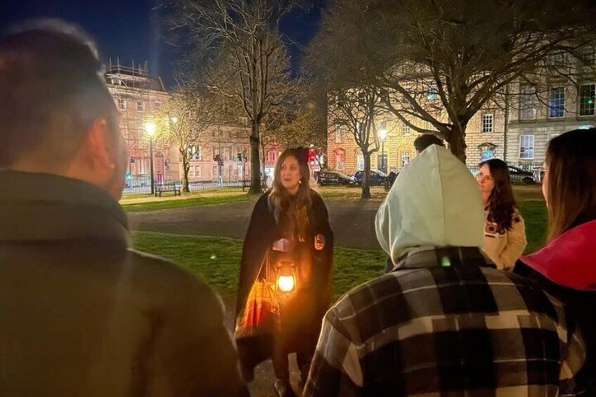 A group of people standing outdoors at night, with trees and a building in the background. 2