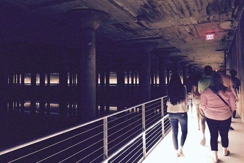 A dimly lit pedestrian walkway with people walking, concrete pillars, and a metal railing. 5
