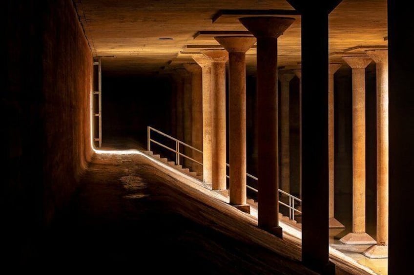 A dimly lit corridor with a staircase, wooden columns, and a metal railing. 4
