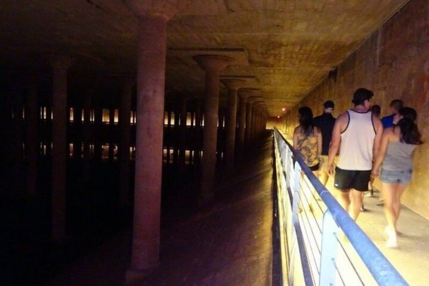 A dimly lit corridor with people walking, concrete pillars, and a railing. 2