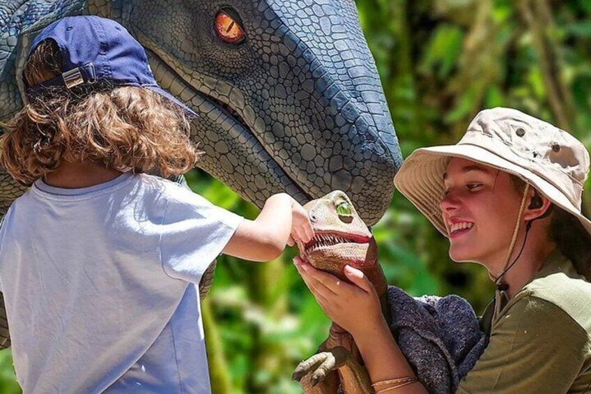 A person holding a small toy dinosaur, another person wearing a hat, and a large dinosaur model. 3