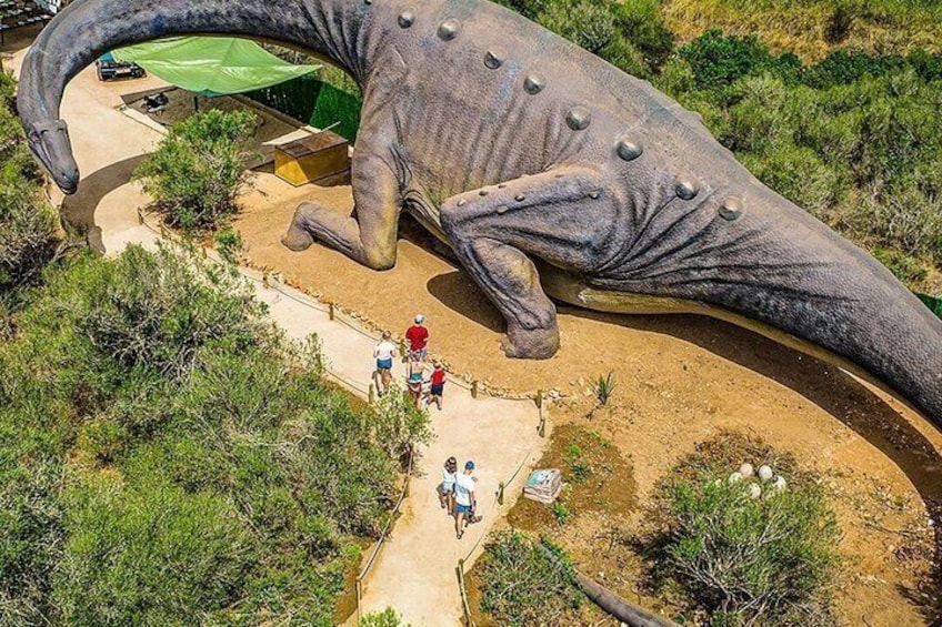 A large dinosaur sculpture in a natural setting with a dirt path and greenery. 2