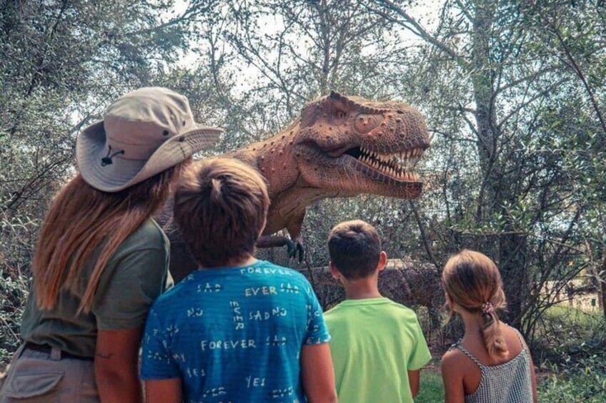 A group of people observing a large dinosaur model outdoors. 1