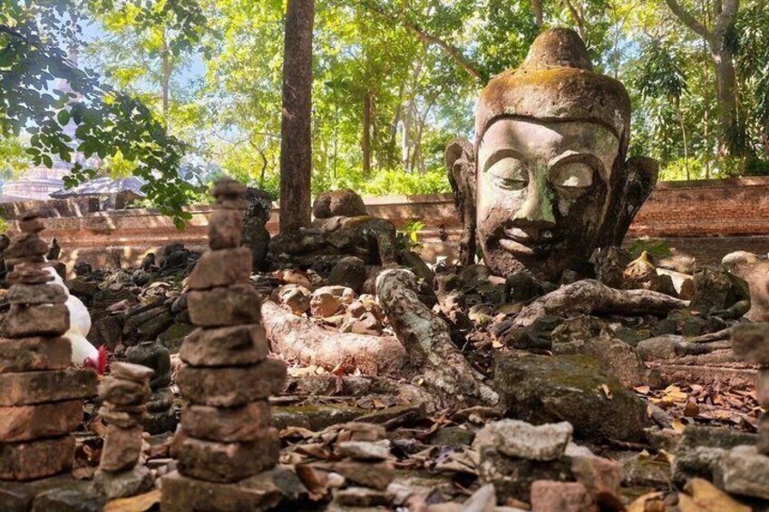 A weathered Buddha statue surrounded by rocks and foliage in a natural setting. 4
