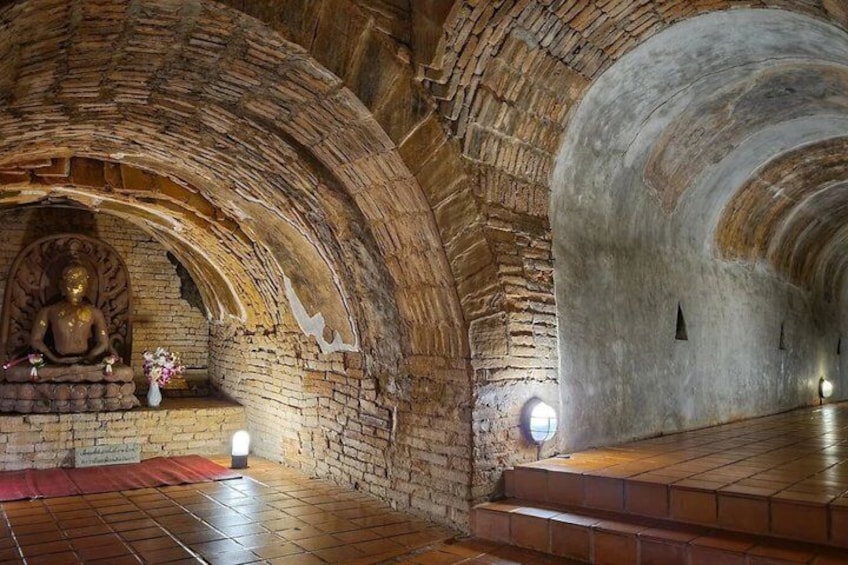 A cave temple interior with a seated Buddha statue, stone walls, and a red mat on the floor. 5