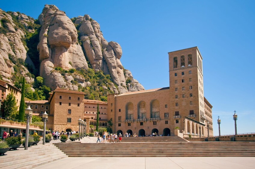 A historic building with a large staircase, a tower, and a rocky mountain backdrop. 1