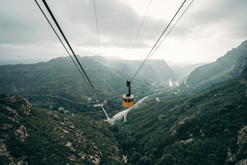A cable car suspended over a mountainous landscape with winding roads below. 3
