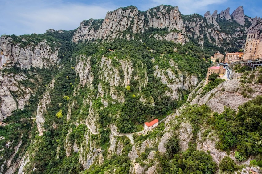 A mountainous landscape with a winding road, a small red-roofed building, and a church on a hill. 4
