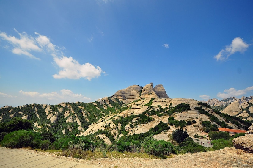 A mountainous landscape with a prominent rock formation, a paved path, and scattered greenery. 2