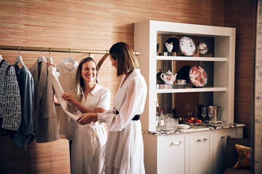 Two people in a room with clothing on a rack and a cabinet with dishes. 4