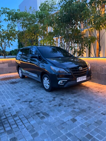 A black minivan parked on a paved area with trees and a building in the background. 4
