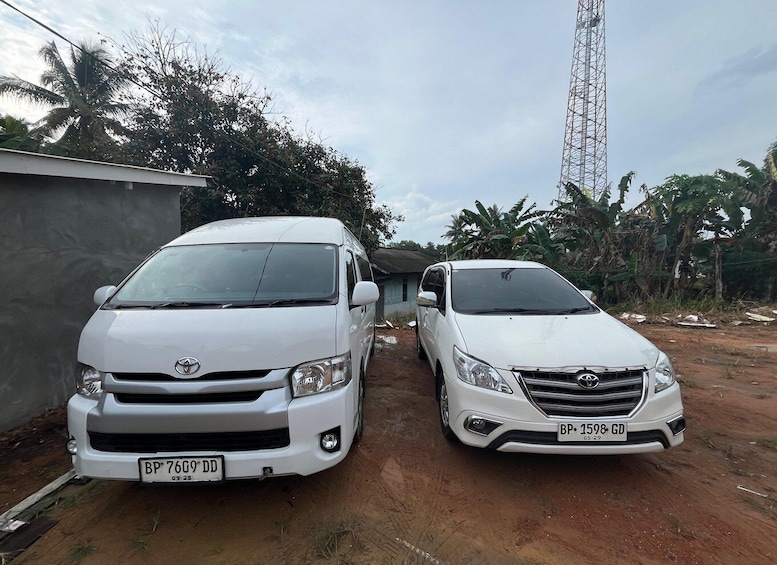 Two white Toyota SUVs parked on a dirt road with a building and palm trees in the background. 3