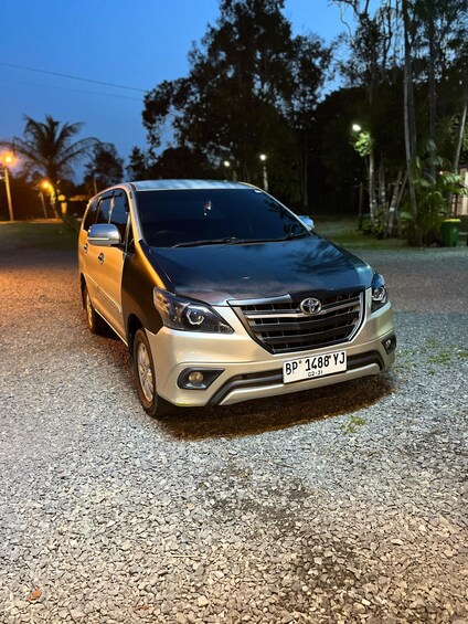A silver SUV parked on a gravel surface at dusk. 2