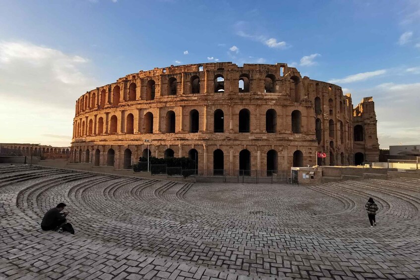 An ancient amphitheater with a circular stone floor and a partially intact structure. 1
