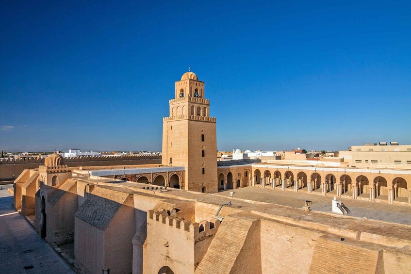 A historic tower with a dome and a minaret, surrounded by a fortified wall with arched passageways. 2