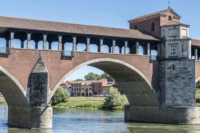 Un puente de piedra con arcos sobre un río, un edificio con torre, y un cielo azul despejado. 5
