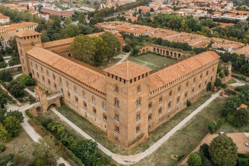 A large, historic building with a courtyard, surrounded by greenery and other buildings. 2
