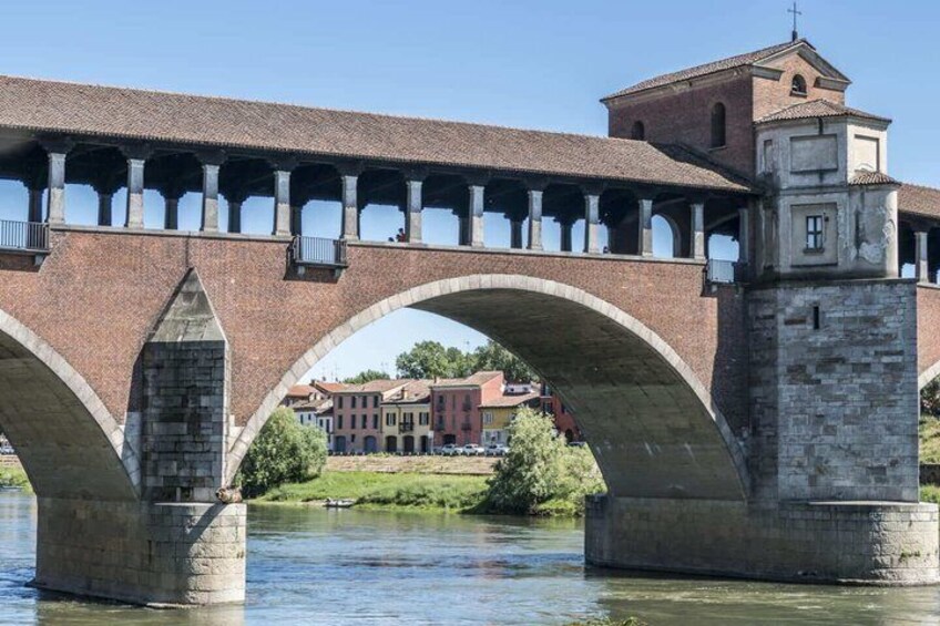 A stone bridge with multiple arches over a river, a building with a red roof in the background, and a tower on the right side. 5