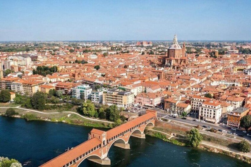 A cityscape with a prominent red-brick bridge over a river, surrounded by historic buildings and a large domed church. 1